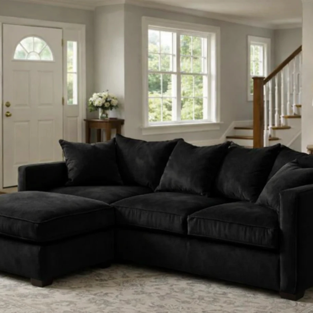 Black jumbo cord corner sofa with chaise section and matching scatter cushions in a modern living room.
