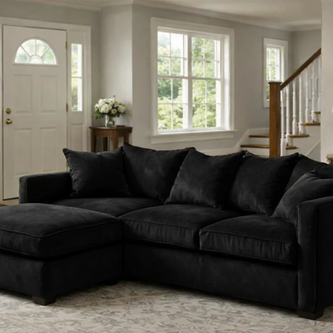 Black jumbo cord corner sofa with chaise section and matching scatter cushions in a modern living room.